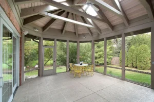 Screened-in hexagonal sunroom with vaulted wood ceiling, ceiling fan, and tiled floor, installed by All Star Sunrooms.
