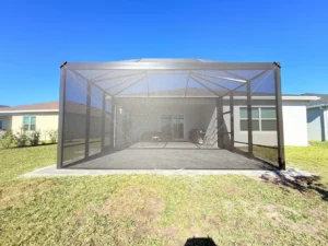 Wide-angle view of a completed pool and patio screen enclosure under a clear blue sky.